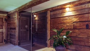 A wooden interior with a glass door leading to a shower area, a potted plant, and a wall-mounted light fixture.