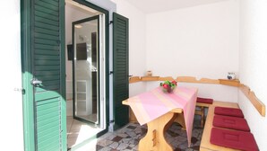 Un petit espace extérieur aménagé avec une table et des bancs, une porte donnant sur une pièce et un sol carrelé.
