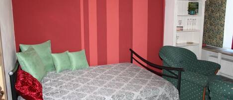 A bedroom with a bed, green armchair, and a white cabinet.