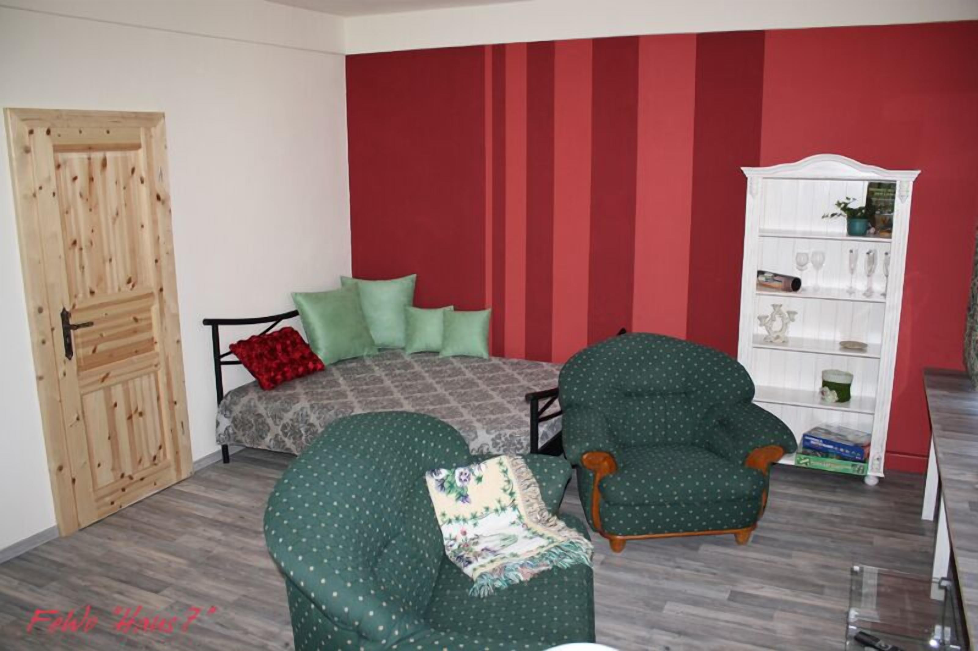 A bedroom with a bed, a green armchair, a white shelving unit, and a wooden door.