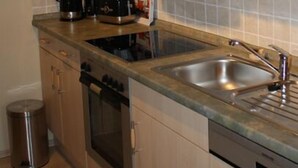 A kitchen with wooden cabinets, a stainless steel sink, a stove, and a trash can. - cozy, quiet apartment near Spreewald, central location, pets welcome (Neupetershain)