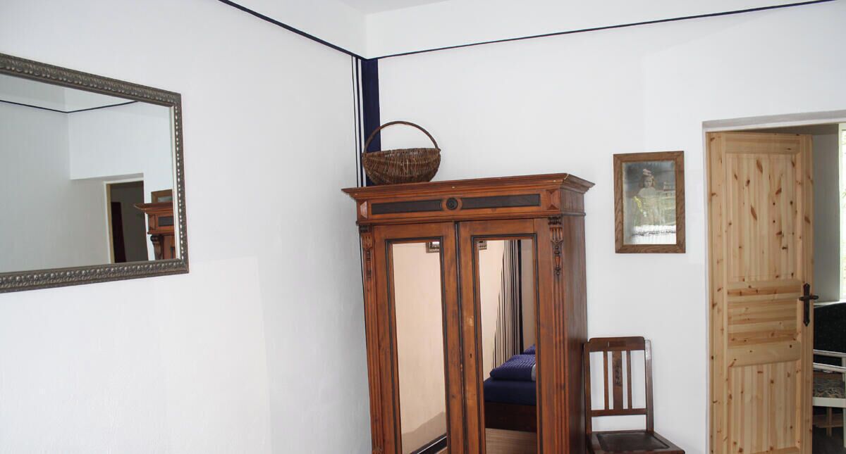 A bedroom with a bed, a wooden wardrobe, a chair, a mirror, and a door.
