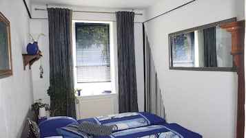 Un dormitorio con cama, una ventana con cortinas, un espejo y una planta.