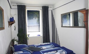 A bedroom with a bed, a window with curtains, a mirror, and a plant.