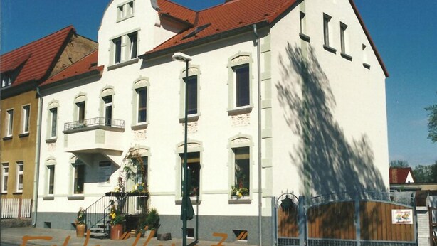A two-story building with a red-tiled roof, white walls, and a balcony with potted plants. - cozy, quiet apartment near Spreewald, central location, pets welcome (Neupetershain)