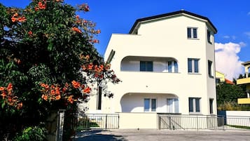 A two-story building with a flat roof, a balcony on the second floor, and a gated entrance.