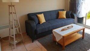A living room with a dark blue sofa, two yellow cushions, a wooden coffee table, a white lamp, and a painting on the wall. - Very nice vacation home, top location, only 50 m to the beach, close to the harbor. 6 persons (Gruissan)