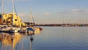 A marina with multiple sailboats docked, a building with a staircase, and calm water reflecting the boats. - Very nice vacation home, top location, only 50 m to the beach, close to the harbor. 6 persons (Gruissan)