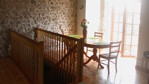 A rustic room with a stone wall, wooden floor, a wooden staircase, a dining table with chairs, and a large window. - Holiday home in one of the most unspoilt landscapes in France. (Chaspinhac)