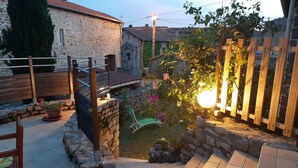 A stone patio with a wooden fence, a bench, and a small garden area with flowers and a lamp post. - Holiday home in one of the most unspoilt landscapes in France. (Chaspinhac)
