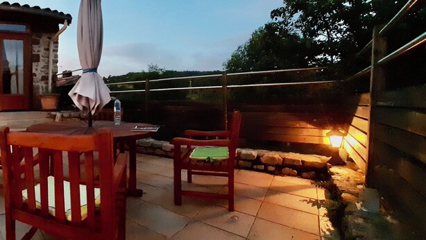 A stone house with a wooden deck, a patio with chairs, and a table. - Holiday home in one of the most unspoilt landscapes in France. (Chaspinhac)