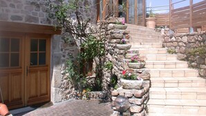 A stone house with a wooden door and windows, a stone staircase, and a small garden with plants and flowers. - Holiday home in one of the most unspoilt landscapes in France. (Chaspinhac)