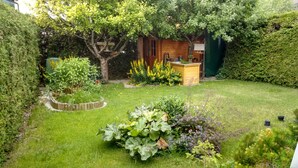 Een verzorgde tuin met een houten tuinhuis, verschillende planten en een kleine boom.