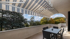 Un patio techado al aire libre con una mesa y sillas, con vistas a un paisaje pintoresco con árboles y la ciudad a lo lejos.