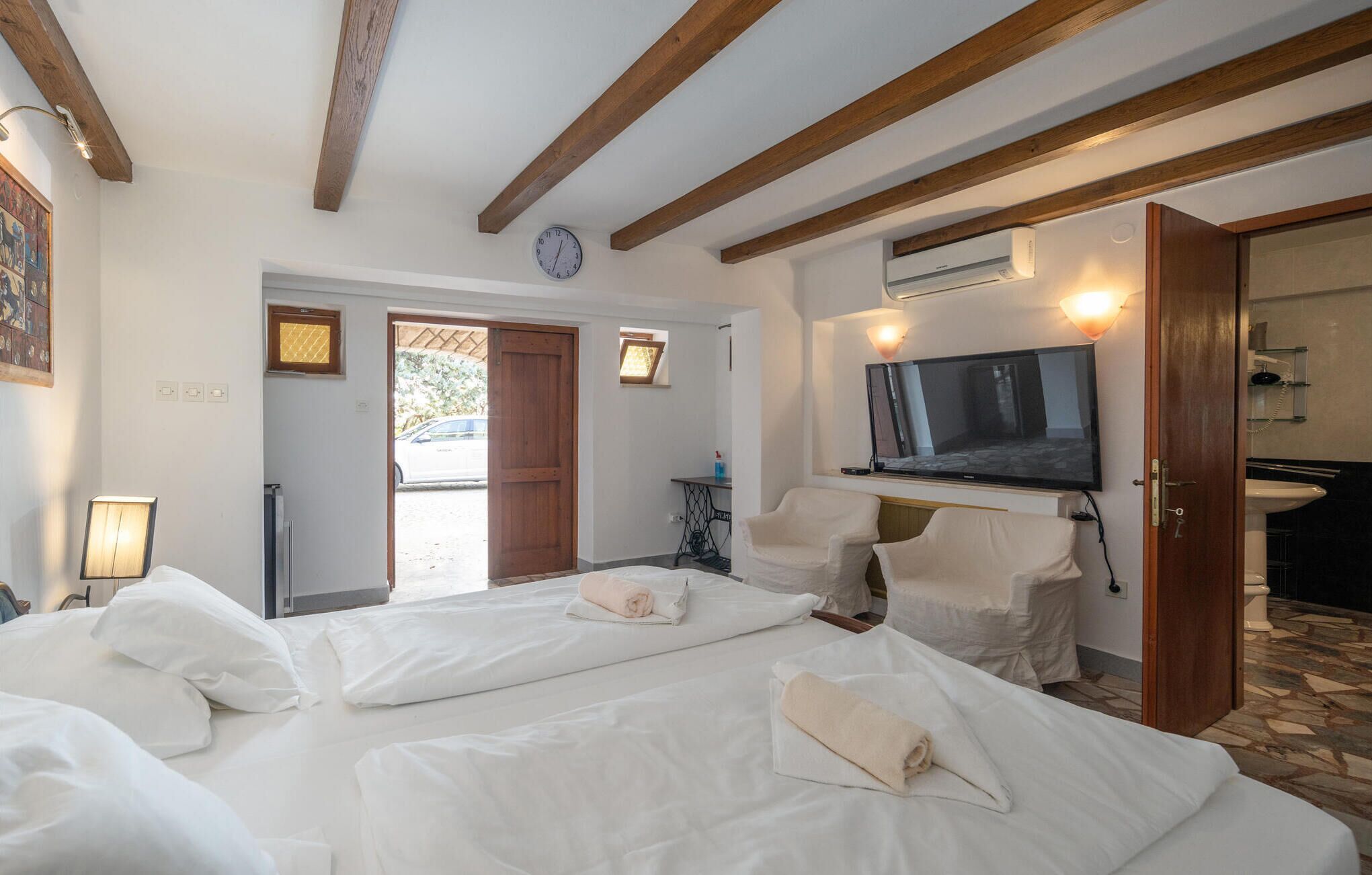 A hotel room with two beds, a television, a bathroom, and a view of the outside.
