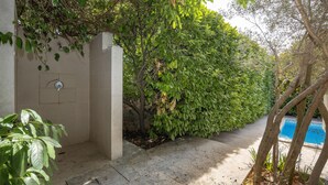 Un camino de hormigón que lleva a una zona de piscina, rodeada de exuberante follaje verde y un muro de piedra.