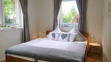 Un dormitorio ordenado con una cama de madera, una mesita de noche con lámpara y una ventana con cortinas.