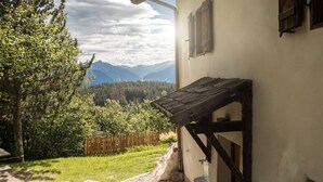 A rustic building with a wooden porch, a wooden fence, and a view of mountains and trees.