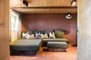 Um quarto aconchegante com teto de madeira, um sofá-cama verde, uma pequena mesa de cabeceira e um abajur.