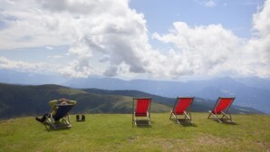 A grassy hill with three red beach chairs and a reclining chair, overlooking a mountainous landscape.