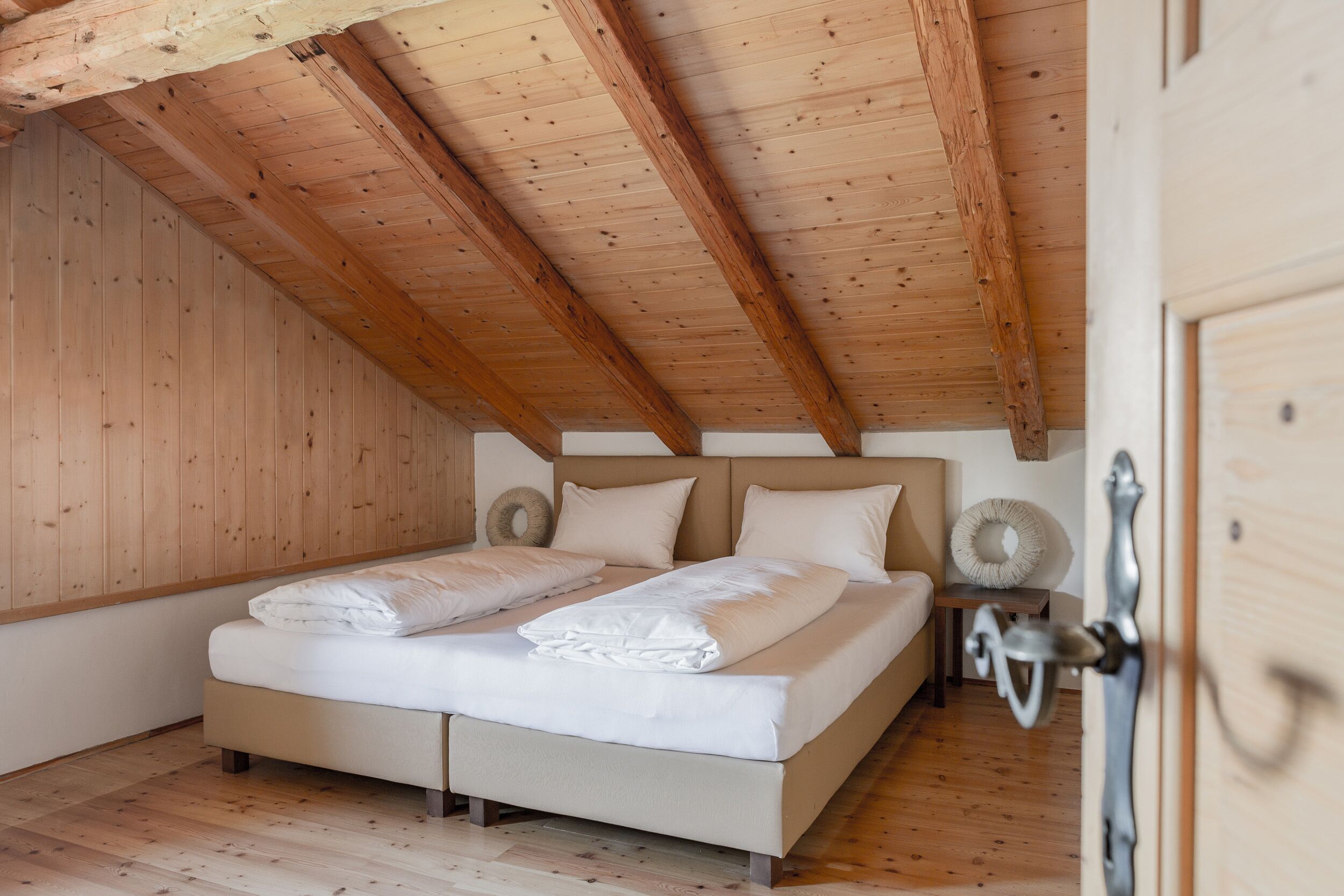 Une chambre avec un plafond en bois, un lit recouvert de draps blancs et une petite table de chevet avec une lampe.