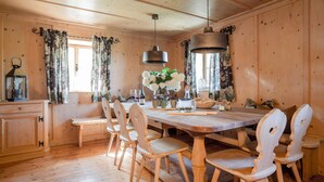 A wooden dining room with a large table, chairs, and hanging pendant lights.