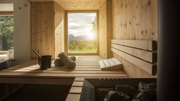 A wooden cabin interior with a large window, a bench, a table, and a small fireplace.