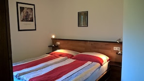 Una cama con colcha a rayas, una mesita de noche con lámpara y dos cuadros en la pared.