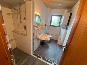 A bathroom with a shower, toilet, sink, and a window.