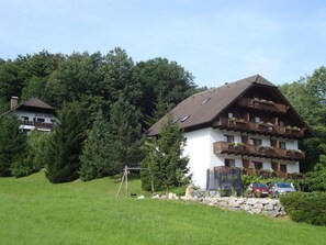 A multi-story building with balconies, surrounded by greenery and a grassy area.