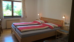 A double bed with a wooden headboard, two bedside tables, a window with curtains, a radiator, and a lamp on the wall.