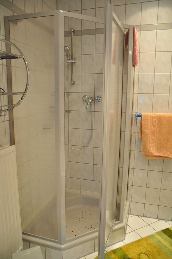 Une cabine de douche dotée d’une porte en verre, d’un pommeau de douche et d’un flexible de douche.