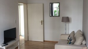 A living room with a television on a stand, a sofa with cushions, a lamp, and a door leading to another room. - Apartment, close to the center and in a quiet location on the floodplain forest (Leipzig)