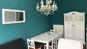A dining area with a white table and chairs, a chandelier, a white cabinet, and a mirror on teal walls. - Apartment, close to the center and in a quiet location on the floodplain forest (Leipzig)