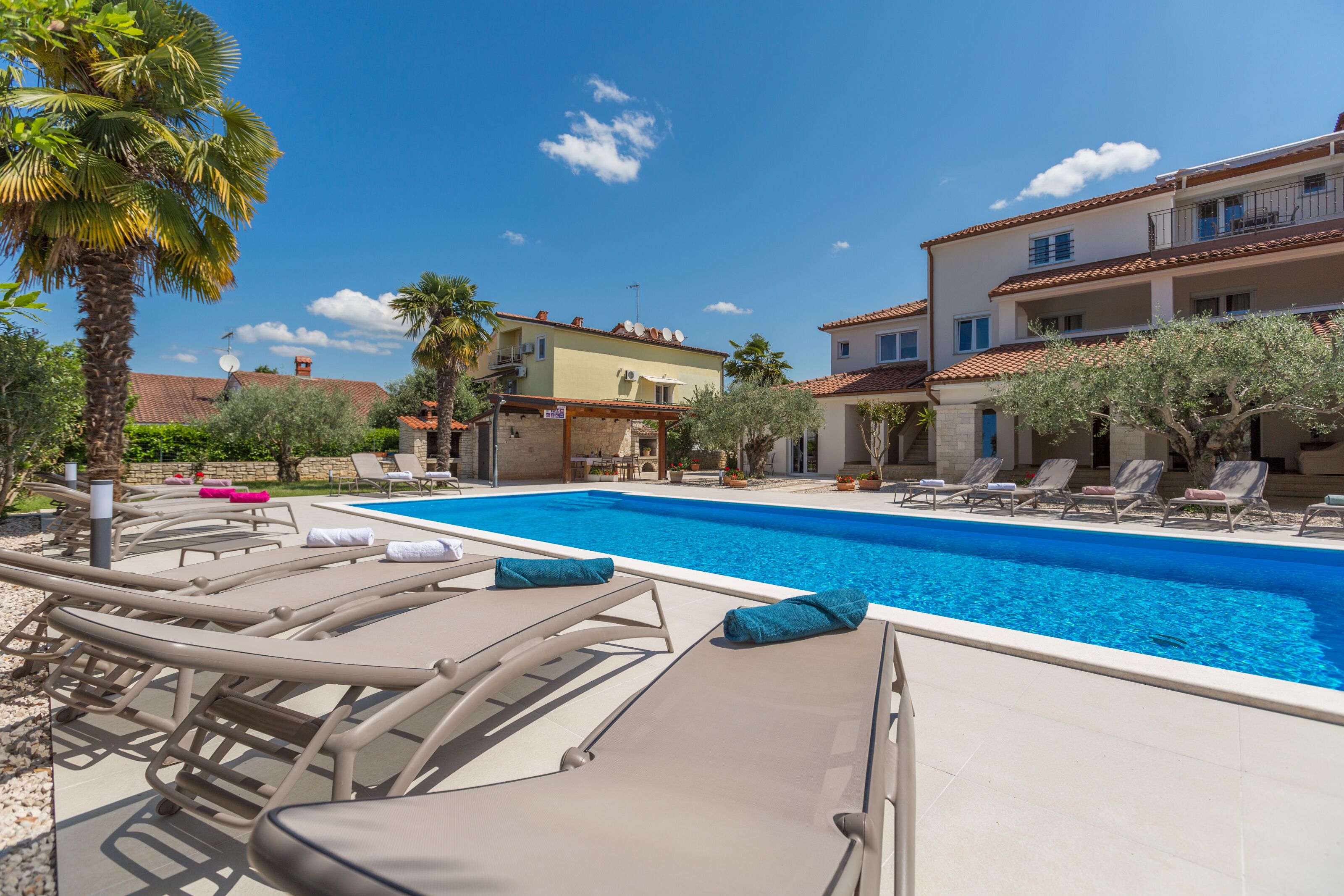 A swimming pool with lounge chairs, palm trees, and buildings in the background.