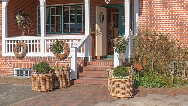 A brick house with a porch, two wicker baskets with plants, and a door.