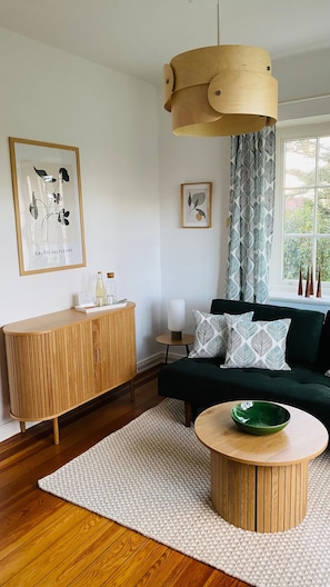 Un salon moderne avec un meuble en bois, une table basse ronde, un canapé foncé agrémenté de coussins à motifs, un luminaire suspendu en bois et des œuvres d’art encadrées accrochées aux murs.