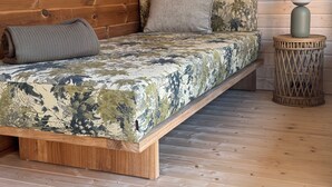 A wooden bed with a camouflage-patterned bedspread, a grey pillow, and a small round side table with a spherical object on top.