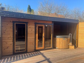 Una cabaña de madera con puertas correderas de vidrio, un jacuzzi y una terraza.