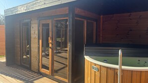 A wooden deck with a hot tub and a covered area with glass doors.