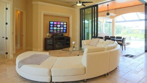 Ein geräumiges Wohnzimmer mit einer gebogenen weißen Couch, einem Flachbildfernseher und einem Deckenventilator.