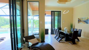 Ein modernes Hotelzimmer mit Glastür zu einem Balkon, einer schwarzen Ledersofa, einem Glastisch, einem Esstisch mit Stühlen und einem großen Fenster mit Blick ins Freie.