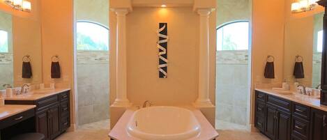 A spacious bathroom with a large bathtub, two sinks, and dark cabinetry.
