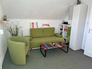 A green sofa, a colorful coffee table, a white cabinet, and a plant in a corner.