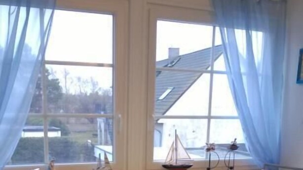 A dining area with a table and two chairs, large windows with curtains, and a view of the outside.