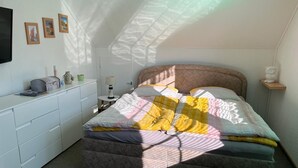 A bedroom with a bed, a desk, and a chair. There are framed pictures on the wall.