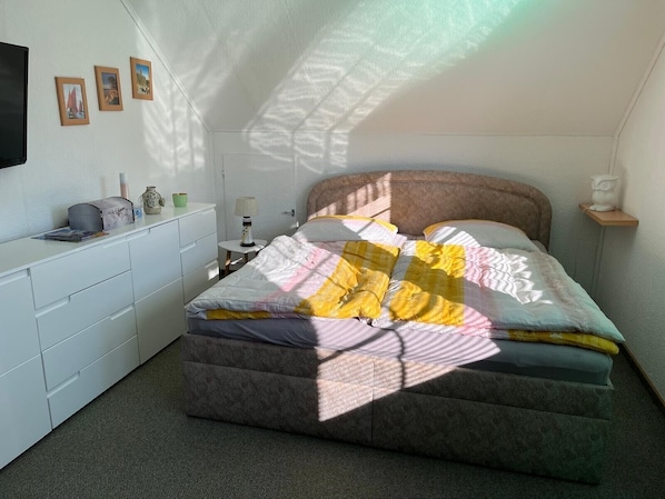 A bedroom with a bed, a desk, and a chair. There are framed pictures on the wall.