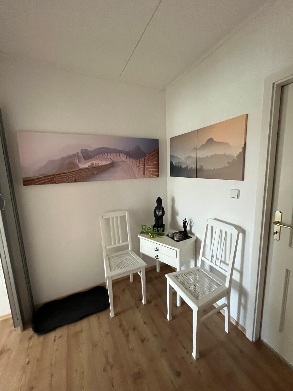Una habitación con dos sillas blancas, un escritorio pequeño blanco y dos cuadros colgados en la pared.