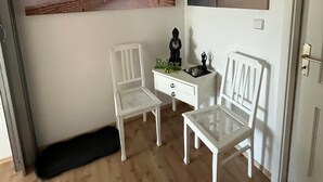 A room with two white chairs, a small white desk, and two wall-mounted paintings.
