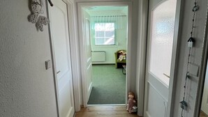 A narrow hallway with wooden flooring, white walls, and a door leading to a room with a window.
